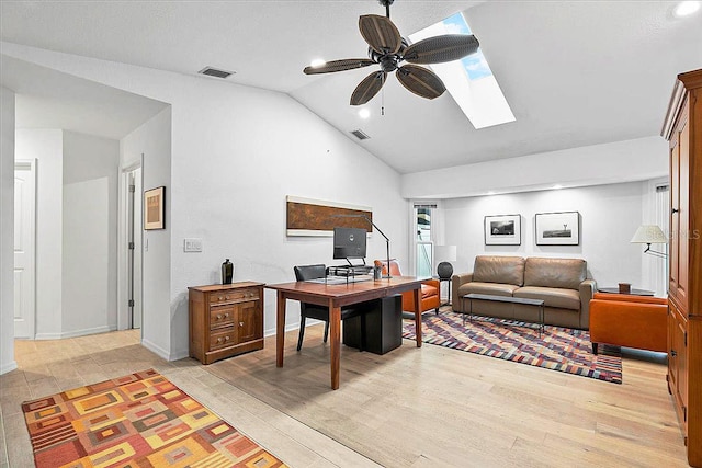 home office featuring ceiling fan, vaulted ceiling with skylight, and light wood-type flooring