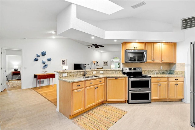 kitchen with sink, ceiling fan, stainless steel appliances, vaulted ceiling with skylight, and kitchen peninsula