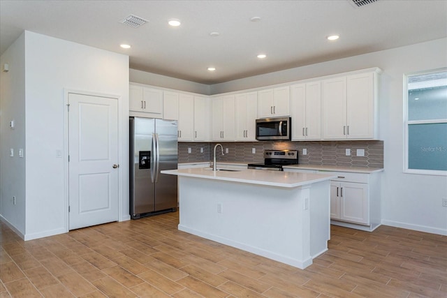 kitchen featuring stainless steel appliances, a kitchen island with sink, white cabinets, and light hardwood / wood-style floors