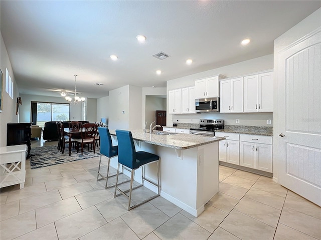 kitchen with pendant lighting, appliances with stainless steel finishes, light stone counters, an island with sink, and white cabinets