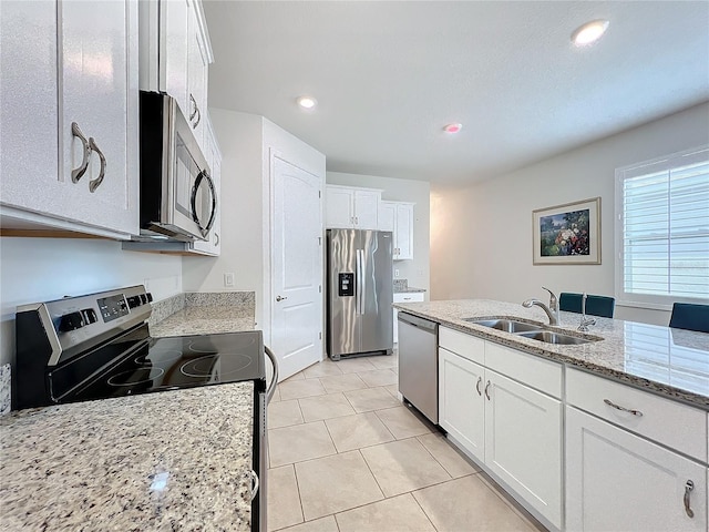 kitchen with stainless steel appliances, white cabinetry, sink, and light stone counters