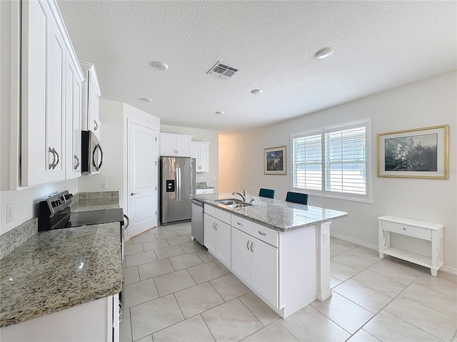 kitchen featuring sink, white cabinetry, appliances with stainless steel finishes, light stone countertops, and a kitchen island with sink