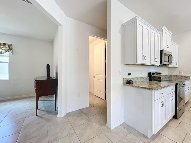 kitchen featuring stainless steel appliances, white cabinetry, light tile patterned flooring, and dark stone counters