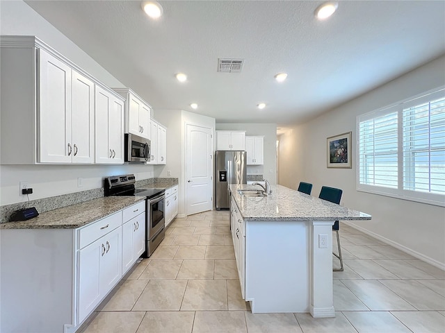 kitchen with white cabinetry, stainless steel appliances, an island with sink, and a breakfast bar