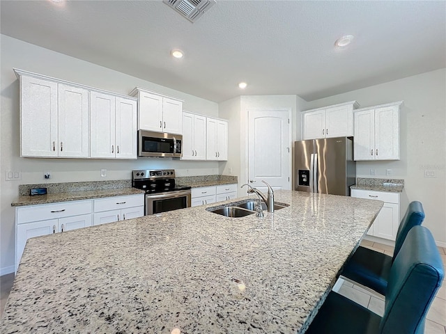 kitchen with white cabinetry, appliances with stainless steel finishes, sink, and a center island with sink