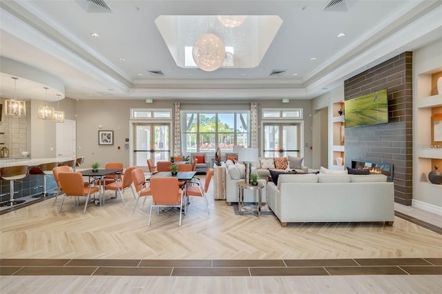 living room with an inviting chandelier, a tray ceiling, a fireplace, and crown molding