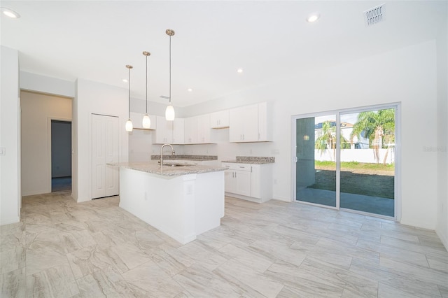 kitchen with an island with sink, sink, white cabinets, hanging light fixtures, and light stone countertops