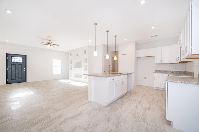 kitchen with sink, light stone countertops, white cabinets, a center island with sink, and decorative light fixtures