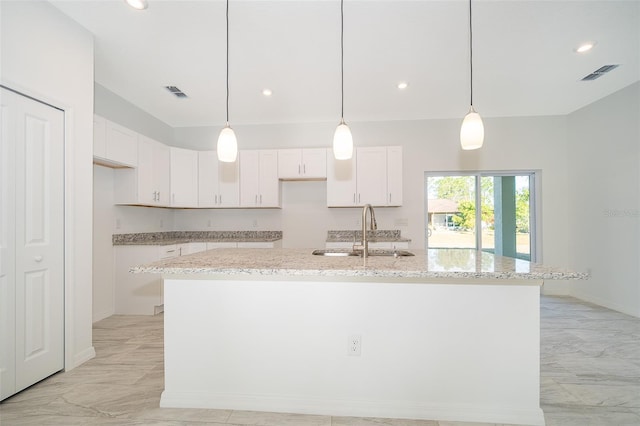 kitchen featuring sink, light stone countertops, a kitchen island with sink, and white cabinets