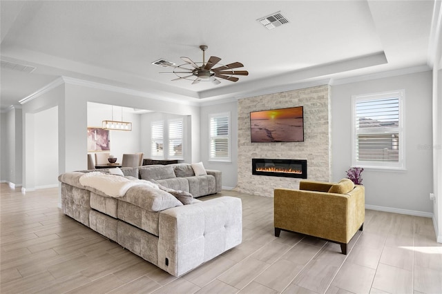 living room with a raised ceiling, a stone fireplace, and a wealth of natural light