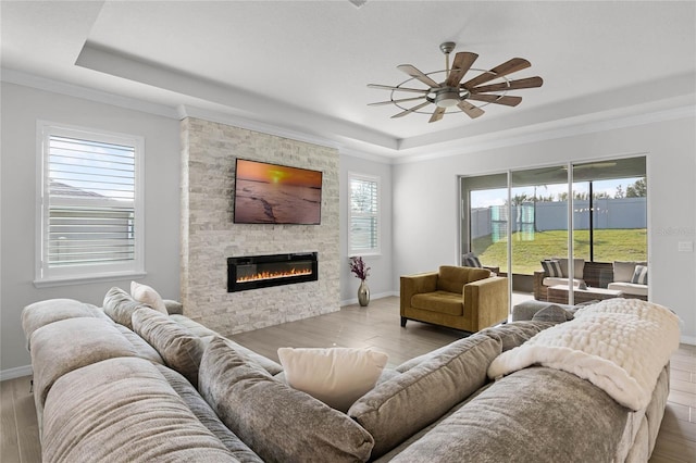 living room with ceiling fan, a fireplace, a raised ceiling, and light hardwood / wood-style flooring