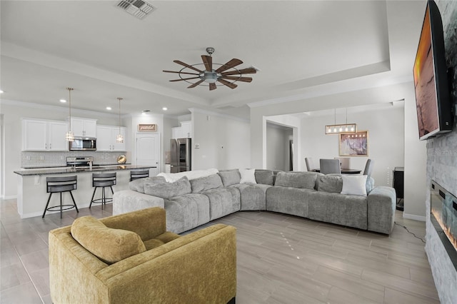 living room with crown molding, ceiling fan, a raised ceiling, and sink