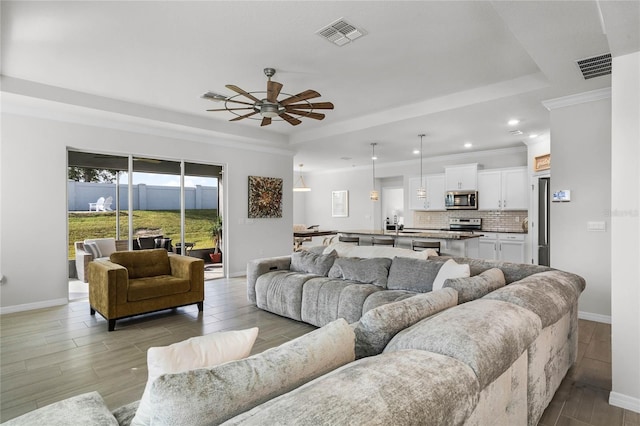 living room featuring ceiling fan, ornamental molding, a tray ceiling, and light hardwood / wood-style floors