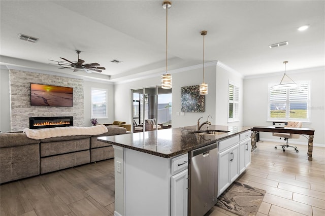 kitchen with white cabinetry, an island with sink, decorative light fixtures, stainless steel dishwasher, and dark stone counters