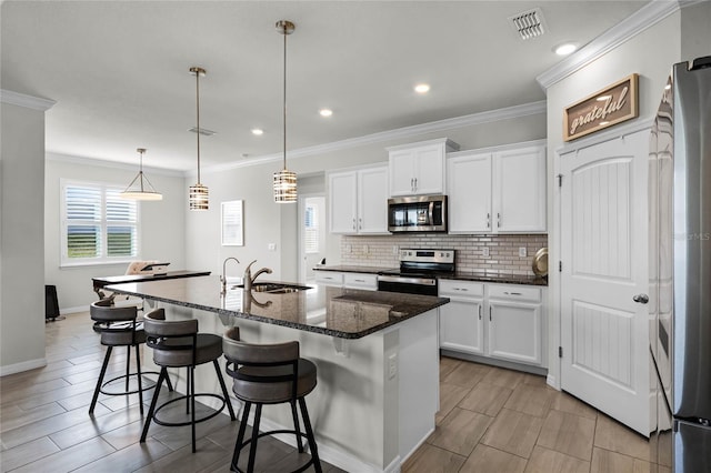 kitchen with appliances with stainless steel finishes, pendant lighting, a center island with sink, and white cabinets