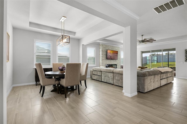 dining area featuring a healthy amount of sunlight, a tray ceiling, a stone fireplace, and light hardwood / wood-style flooring