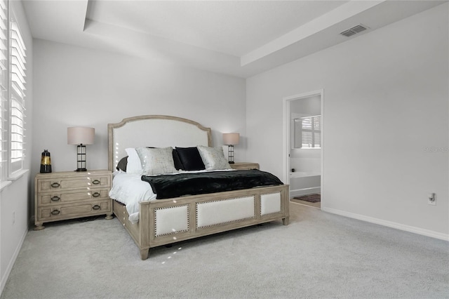 carpeted bedroom featuring ensuite bathroom and a raised ceiling