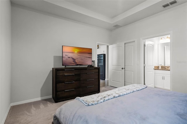 bedroom with light carpet, connected bathroom, and a raised ceiling