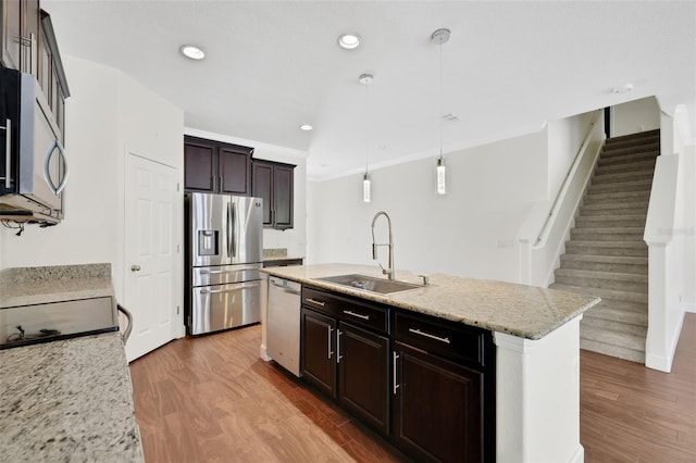 kitchen with sink, light stone counters, decorative light fixtures, appliances with stainless steel finishes, and a kitchen island with sink