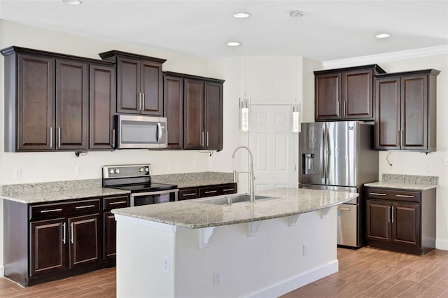 kitchen featuring sink, appliances with stainless steel finishes, a kitchen bar, a center island with sink, and light wood-type flooring