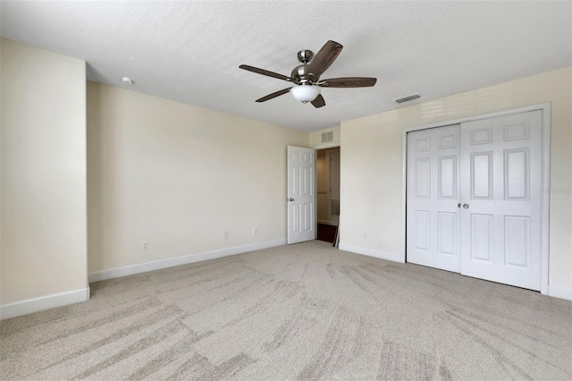 unfurnished bedroom featuring ceiling fan, light colored carpet, a textured ceiling, and a closet