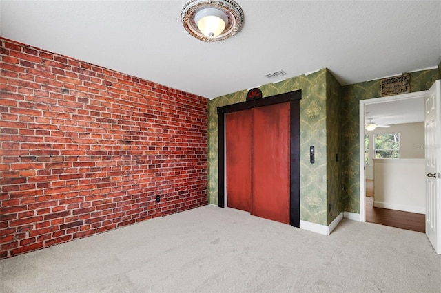 unfurnished bedroom with carpet floors, a textured ceiling, brick wall, a closet, and elevator