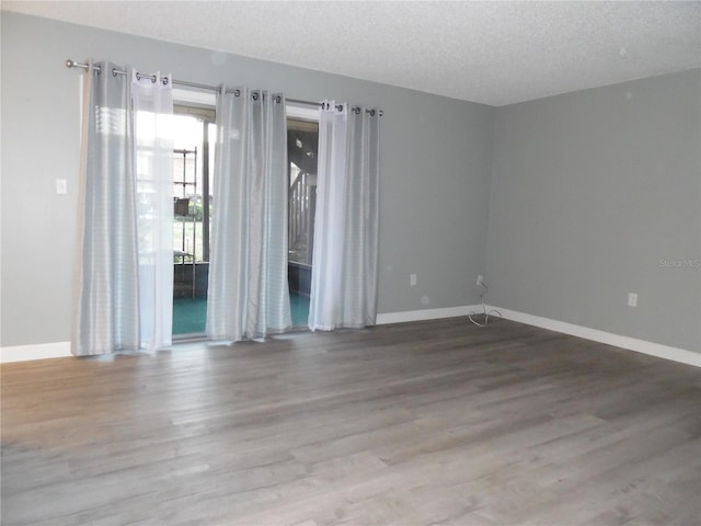 spare room with a textured ceiling, baseboards, and wood finished floors