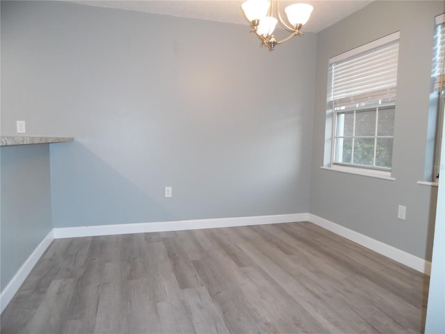 unfurnished dining area with baseboards, a chandelier, and wood finished floors