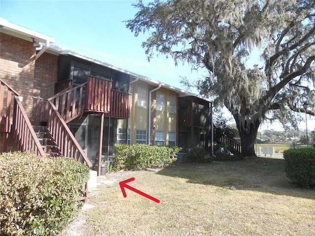 rear view of property featuring brick siding, a yard, a deck, and stairs