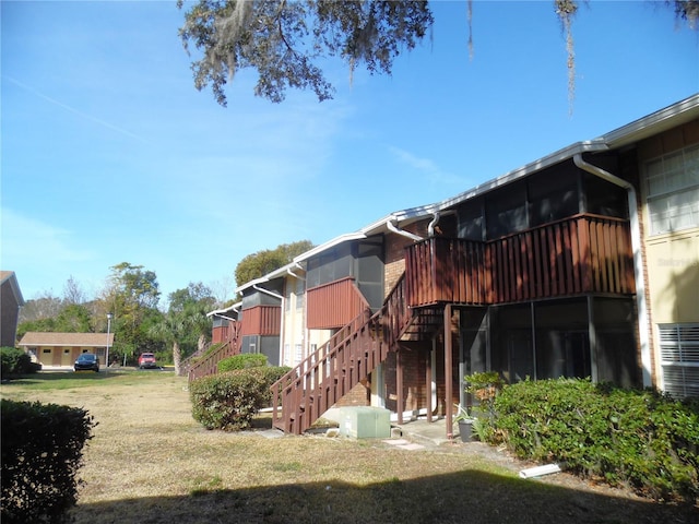 view of side of property featuring stairs, a lawn, and a sunroom