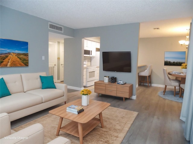 living room featuring a textured ceiling, visible vents, a chandelier, and wood finished floors