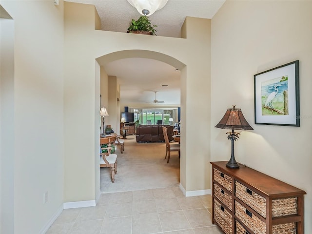 hall featuring light colored carpet, light tile patterned flooring, arched walkways, and baseboards