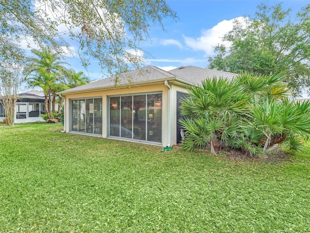 rear view of property with a sunroom, a yard, and stucco siding