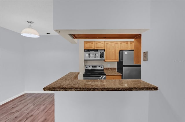 kitchen with appliances with stainless steel finishes, light brown cabinetry, hanging light fixtures, light hardwood / wood-style floors, and kitchen peninsula