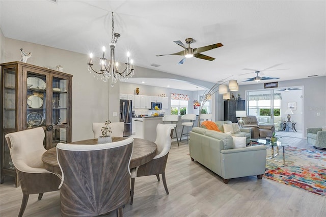 dining room with ceiling fan with notable chandelier, vaulted ceiling, and light hardwood / wood-style flooring