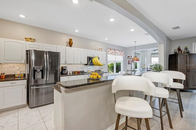 kitchen featuring decorative light fixtures, white cabinetry, backsplash, dark stone counters, and stainless steel refrigerator with ice dispenser