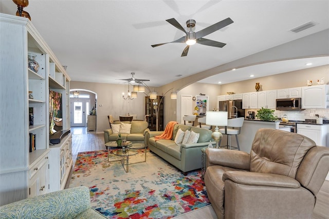 living room with ceiling fan with notable chandelier and light hardwood / wood-style flooring