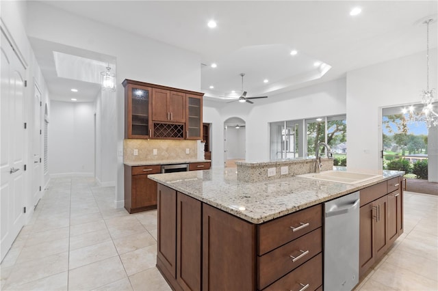 kitchen featuring sink, tasteful backsplash, stainless steel dishwasher, a raised ceiling, and an island with sink