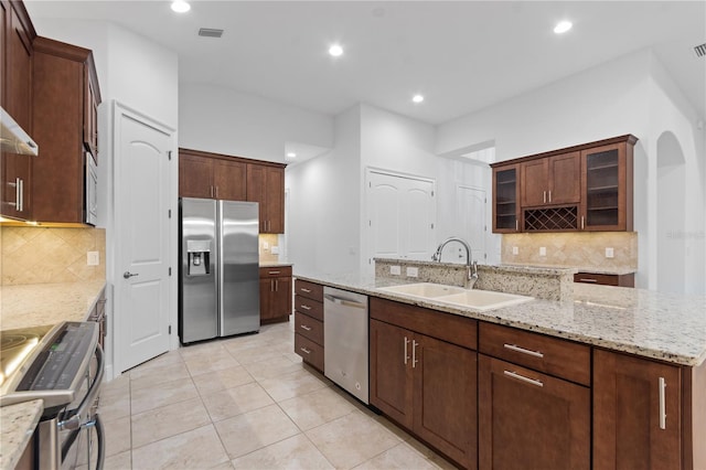 kitchen with stainless steel appliances, light stone countertops, sink, and a center island with sink