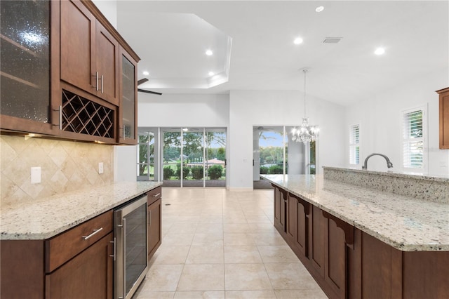 kitchen with tasteful backsplash, decorative light fixtures, light stone countertops, and beverage cooler