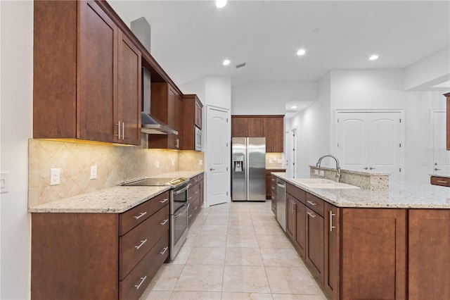 kitchen featuring sink, light stone counters, a center island with sink, appliances with stainless steel finishes, and wall chimney range hood