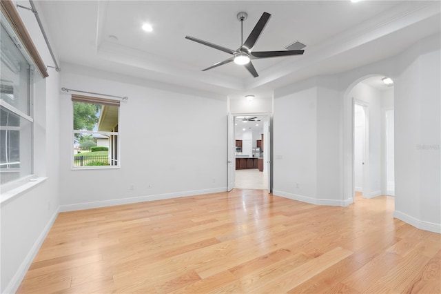 empty room with a tray ceiling, ornamental molding, light hardwood / wood-style floors, and ceiling fan