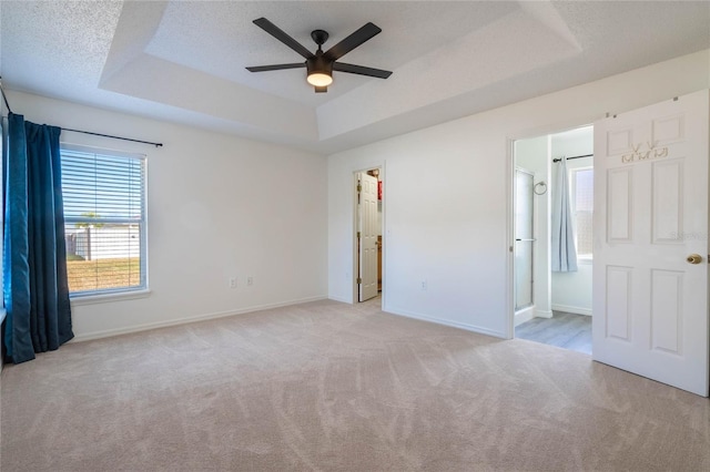 interior space featuring connected bathroom, a walk in closet, a raised ceiling, light carpet, and a textured ceiling