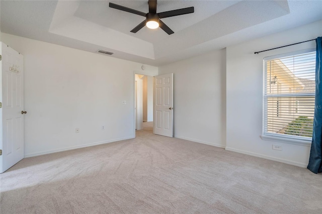 carpeted spare room featuring ceiling fan and a tray ceiling