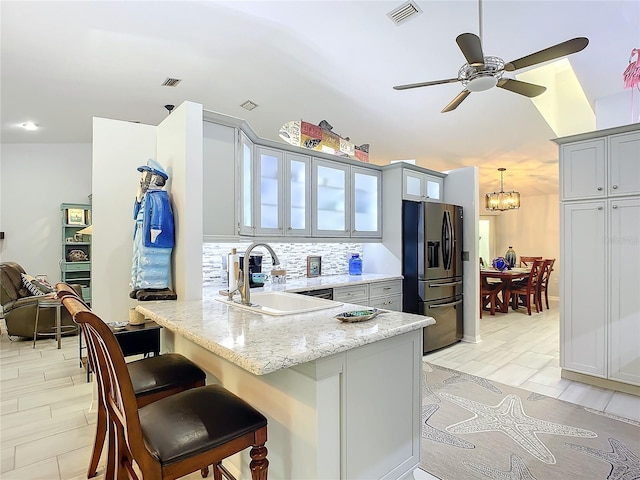 kitchen with sink, a breakfast bar area, stainless steel fridge, gray cabinets, and backsplash