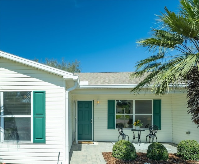 property entrance with covered porch and a shingled roof