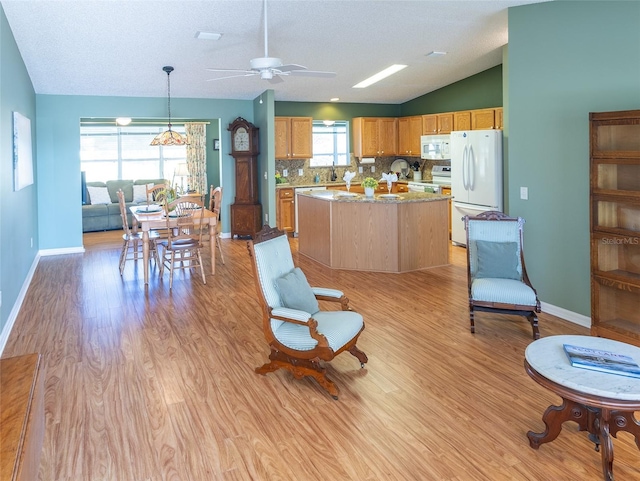 kitchen with a center island, hanging light fixtures, vaulted ceiling, light wood-type flooring, and white appliances