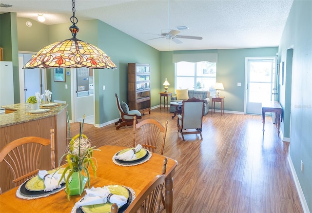 dining area featuring a ceiling fan, vaulted ceiling, a textured ceiling, wood finished floors, and baseboards