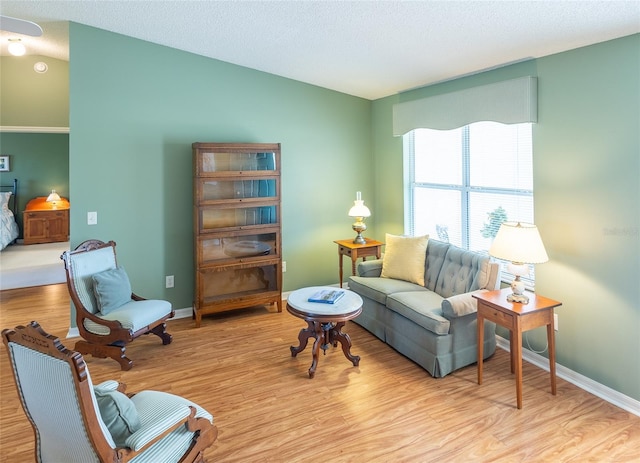 living area with a textured ceiling, light wood-type flooring, and baseboards