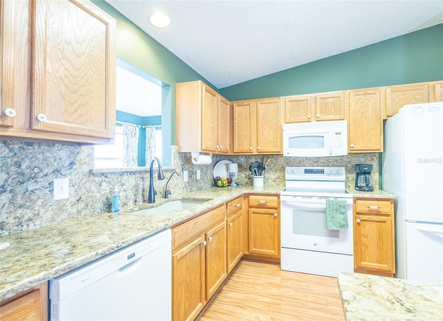 kitchen with white appliances, decorative backsplash, lofted ceiling, light stone counters, and a sink